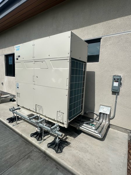 Daikin VRV outdoor heat pump mounted on a pipe stand with insulated refrigerant line set and electrical disconnect
