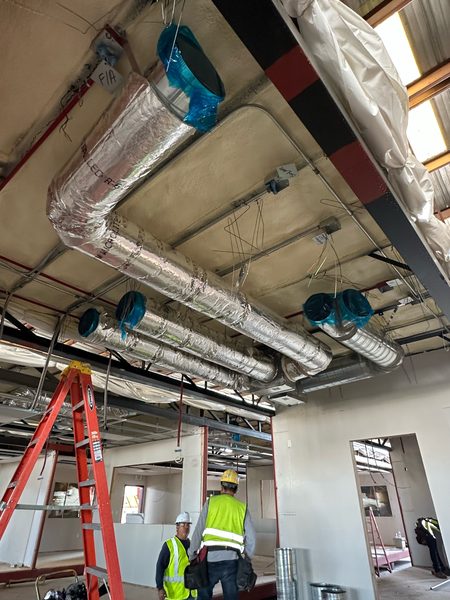 Insulated round and flex ductwork roughed in overhead while workers in hard hats and safety vests work below