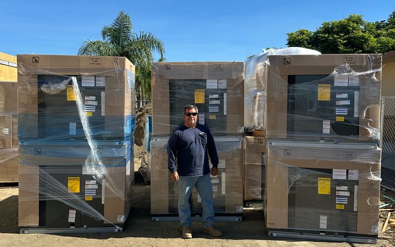 Six shrink-wrapped packaged HVAC units delivered to a job site and staged for installation