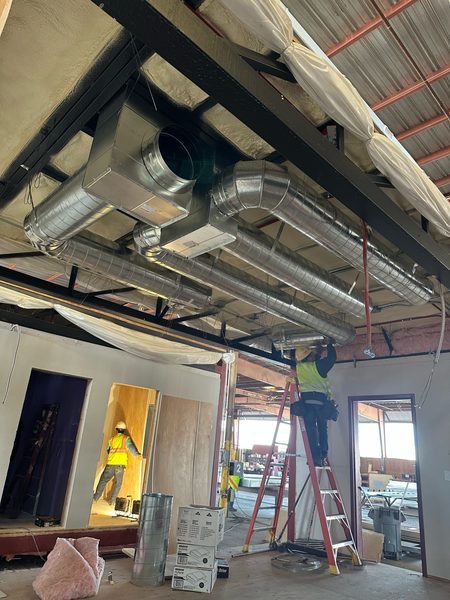 Spiral supply duct and plenum box being installed inside a modular building unit in a factory setting