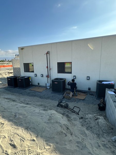 Technician connecting split-system condensing units along the wall of a new modular building