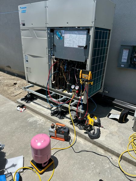 Technician starting up a Daikin VRV unit with refrigerant gauges, vacuum pump and refrigerant tank connected